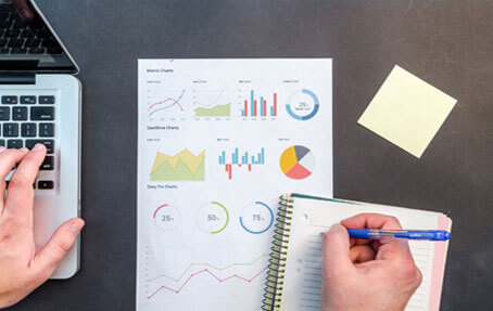 a person working on business data analysis, with charts and graphs on paper, a notebook, and a laptop