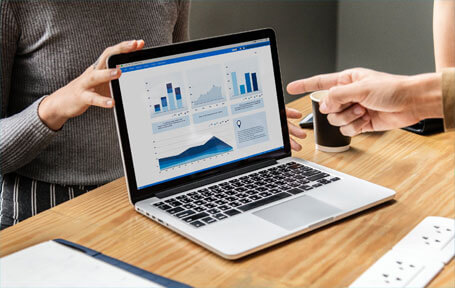 two people discussing data visualizations displayed on a laptop screen, which includes charts and graphs