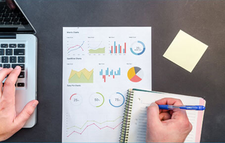 a person working on business data analysis, with charts and graphs on paper, a notebook, and a laptop