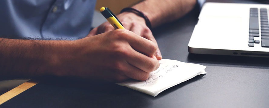 A Person in front of laptop writing on paper.